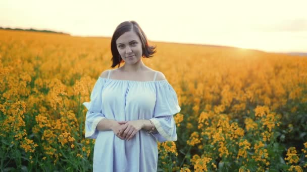 Portret van jonge mooie vrouw in blauwe jurk poseren in koolzaad gele bloemen veld. Lente, zonsondergang licht. — Stockvideo