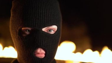 Yanan bir gece yangınının arka planında siyah balaclava genç kadının portresi. Kitlesel mitingler ve ayaklanmalar kavramı