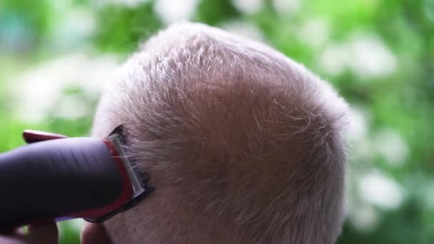 Un uomo che si fa tagliare i capelli dal parrucchiere. Donna barbiere utilizza la macchina per tagliare l'uomo con i capelli grigi. Taglio di capelli all'aperto in estate. Primo piano — Video Stock