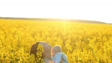 Genç Anne gökyüzüne bebek atar ve gülüyor. Bebek sarı kanola alanında eğlenin. Aşk, Aile, sevinç konsepti