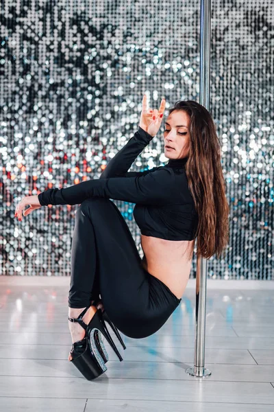 Alluring woman with long hair posing with pylon on shining wall background. Pole-dance, sexy, temptation concept.