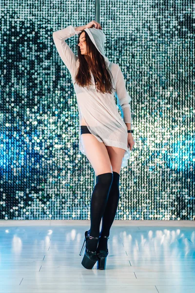 Alluring woman with long hair posing with pylon on shining wall background. Pole-dance, sexy, temptation concept.