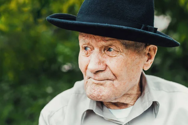 Antiguo retrato de último año. Abuelo con sombrero. Más de 90 años. Retrato: anciano, anciano, solitario, hombre con muchas arrugas en la cara. Primer plano de un anciano pensativo sentado solo al aire libre . — Foto de Stock