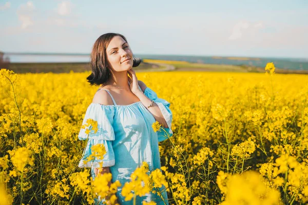 Портрет молодої красивої жінки в блакитній сукні, що позує на полі жовтих квітів ріпаку. Весняний час, захід сонця . — стокове фото