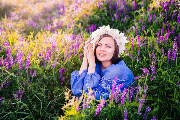 Ung vacker kvinna med blomkrans sitter i lila fält. Porträtt av flicka i blå kläder. — Stockfoto