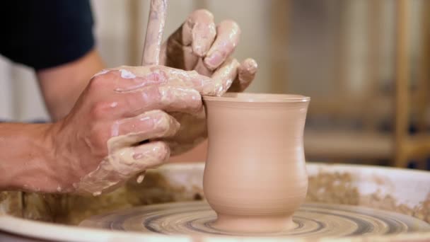 Ervaren potter vormen de klei product - jug - met aardewerk tools. Close up van mannelijke handen werken op potters wiel. Schot van half afgewerkte keramische vaas spinnen op jigger. — Stockvideo