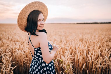 Retro tarzı elbise ve şapka buğday altın alanda poz kadın. Seyahat, hasat, doğa, eski moda konsepti.