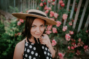 Zarif genç kadın retro tarz elbise ve şapka gül arka plan üzerinde poz. Eski Avrupa kırsalGüzel kız.