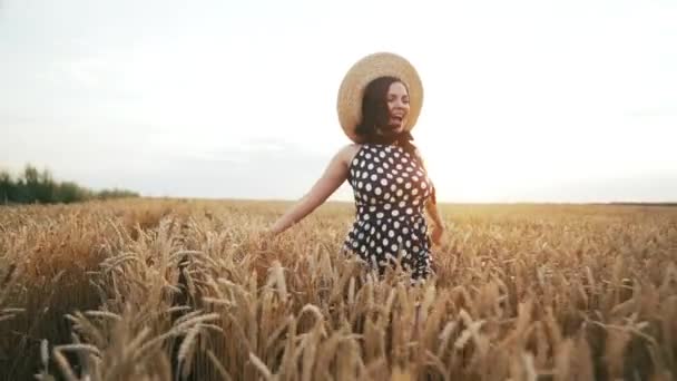 Vrolijke vrouw in stro hoed loopt in tarwe gouden veld tijdens zonsondergang. Meisje met plezier, glimlachend. Vrijheid, vreugde, geluk concept. — Stockvideo