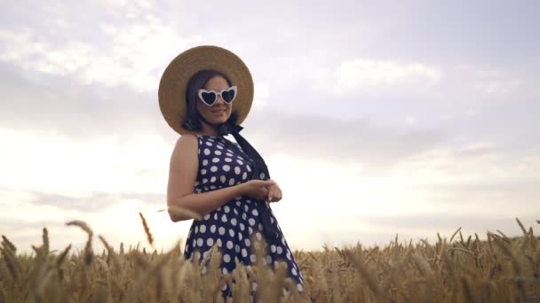 Potret wanita di ladang gandum. Gadis berpakaian retro dengan topi jerami, kacamata hitam berbentuk hati, gaun hitam. Perjalanan, fashion, konsep alam — Stok Video