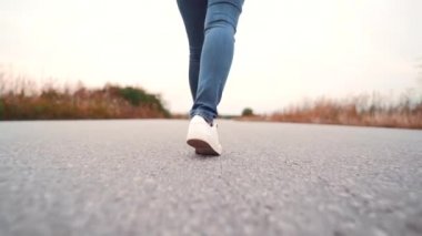 Denim ve trendy ayakkabı genç kadın asfalt pürüzsüz yolda boyunca yürüyor. Modern spor ayakkabı kavramı, seyahat, yürüyüş. Arka çekim.