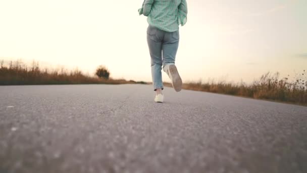 Woman in denim and trendy shoes running along on asphalt smooth road.Concept of modern sneakers, travel, jogging. Rear shot. — Stock Video