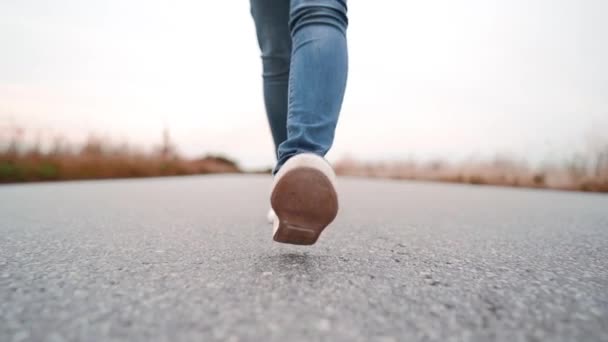 Kot pantolon ve beyaz ayakkabı yabancı kız kamera ileri asfalt pürüzsüz yolda yürüyor. Modern spor ayakkabı kavramı, seyahat, yaz doğada yürüyüş. — Stok video