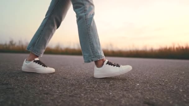 Onherkenbaar vrouw in jeans en witte sneakers loopt langs asfalt weg vooruit. Concept van moderne schoenen, reizen, wandelen in de zomer natuur. Camera scheuten van rechterkant. — Stockvideo