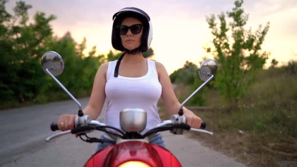 Портрет молодой красивой женщины. Девушка в шлеме и очках сидит на красном ретро скутере на фоне природы . — стоковое видео