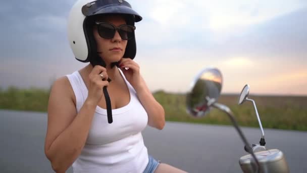 Jonge vrouw zet witte helm op het hoofd en gaat op rit op retro rode scooter op de snelweg in de zomer bij zonsondergang. — Stockvideo