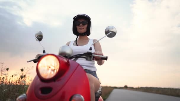 Çekici kız portresi. Beyaz giysiler ve güneş gözlüğü lady gün batımı arka planda kırmızı retro moped üzerinde oturan. — Stok video