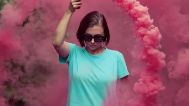 Pembe sis bombası veya el bombası ile genç güzel kadın dramatik karamsar Aydınlatma. Turkuaz tişörtlü kız ve güneş gözlüğü yuvarlak hareketler yapma.
