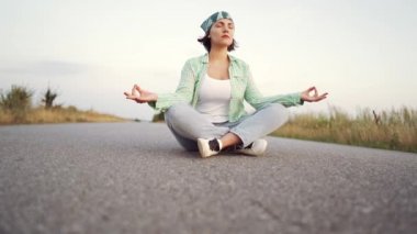 Nilüfer'de meditasyon yapmakta olan genç modakadın çöl kumları arasındaki boş yolda oturuyor. Yoga, din, zen kavramı.