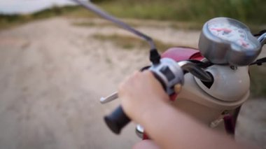 Kırmızı scooter kullanan kadın elleri. Kız country kayalık yol boyunca sürmek. Hızla hareket halinde çekim. Üst yan görünüm.