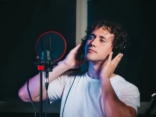 Male vocal artist with curly hair singing alone. Young handsome singer man emotionally writing song in the studio. Recording new melody or album.