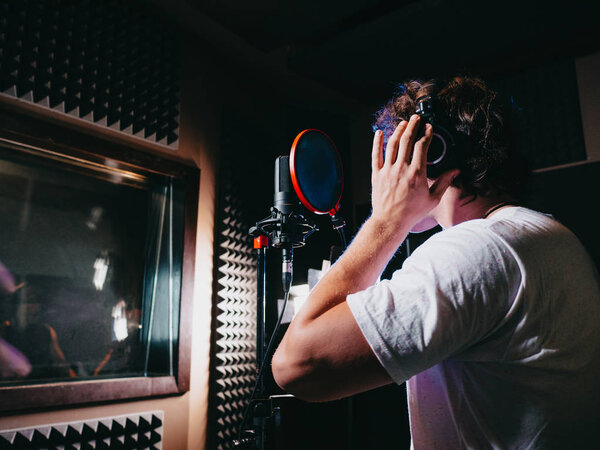 Young handsome singer man puts on headphones in the studio. Recording new melody or album. Male vocal artist with curly hair preparing for working. 