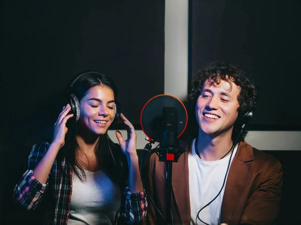 Two young singers performing song in record studio.Professional musician duet recording new album CD.Beautiful couple working and singing near microphone together.