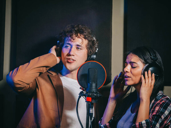 Young team of singers performing song in record studio.Professional musician duet recording new album.Beautiful couple working and singing near microphone together.