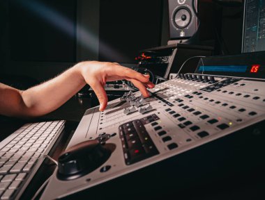 Tanınmayan ses üreticisi veya mühendisi, profesyonel kayıt stüdyosunda karıştırma konsolundaki kaydırma tekerleğidöndürür. Müzisyen yeni bir şarkı üzerinde çalışıyor. Eller kapanır.
