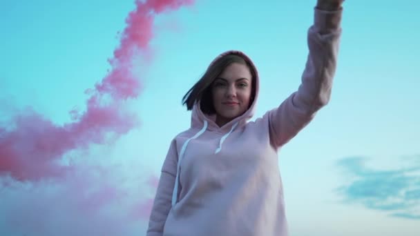 Young pretty woman with pink smoke bomb or grenade on sunset sky background. — Stock Video