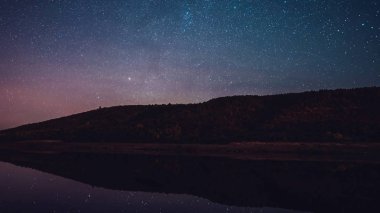 Geceleri dağ ve nehir üzerinde yıldızlı gökyüzü. Takımyıldızlar ve gezegenler 