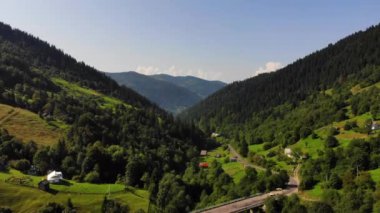 Aerial.Drone çarpıcı dağ doğası üzerinde geriye doğru uçar. Avrupa'da Karpat dağları.Köydeki yükseklikten görünüm, gelişmiş altyapı, köprü, yol. 