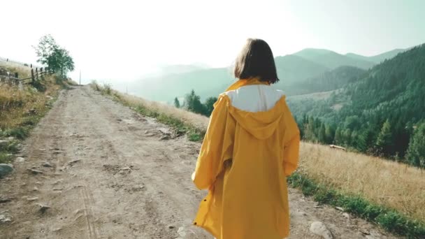 Sarı yağmurluklu kadın yol dışında köyde yürüyor. Karpat dağlarında sabahın erken saatlerinde doğa. Seyahat konsepti — Stok video