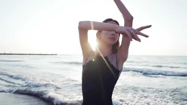 Bailarina bailando en vestido de seda negro en terraplén cerca del océano o el mar al amanecer o al atardecer. Retrato de mujer joven con cabello largo practicando ejercicios clásicos con emociones. — Vídeos de Stock