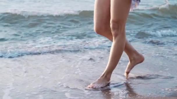 Ноги кавказской девушки в платье и гуляющей босиком мокрым песчаным пляжем. Медленное движение. Женщина проходит мимо камеры — стоковое видео