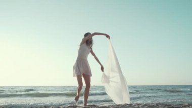 Genç güzel balerin rüzgarda çırpınan büyük ipek kumaş ile deniz kıyısında bale dans. Doğada hassasiyet, hafiflik, sanat ve yetenek kavramı