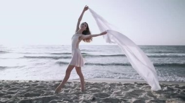 Genç güzel balerin rüzgarda çırpınan büyük ipek kumaş ile deniz kıyısında bale dans. Doğada hassasiyet, hafiflik, sanat ve yetenek kavramı