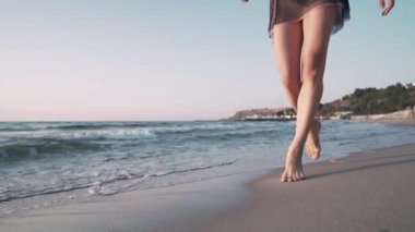 Siyah kısa elbiseli genç, ince bir kızın bacakları kumlu deniz kıyısı gezinti boyunca yürüyor