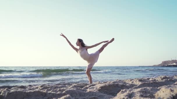 Bailarina bonita esbelta no balé de dança vestido branco no mar ou praia de areia do oceano na luz da manhã. Conceito de arte, beleza da natureza — Vídeo de Stock