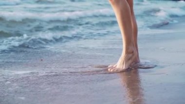 Kumlu deniz kıyısında duran genç, ince bale dansçısı kızın bacakları. Köpük ile sıcak dalgalar tarafından yıkanmış ayaklar
