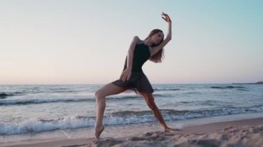 Gün doğumu veya gün batımında okyanus veya deniz yakınında set üzerinde siyah ipek elbise dancing balerin. Uzun saçlı genç kadının silueti duyguları ile klasik egzersizler pratik