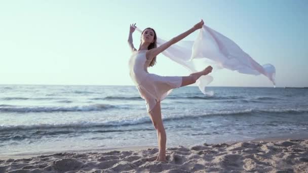 Gymnast står i en svår pose på stranden och rymmer i händerna långa tyg, som segel fladdrande i vinden. Begreppet Dans, ömhet, Balett — Stockvideo