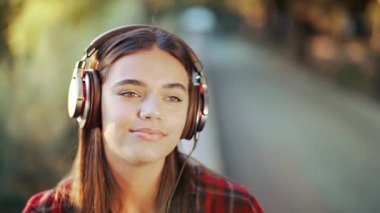 Genç kız kulaklıkla müzik dinliyor. Kırmızı ekose gömlekli kız gülümsüyor, ritimle dans ediyor. Öğrenci hayatı, özgürlük, modern gençlik kavramı.