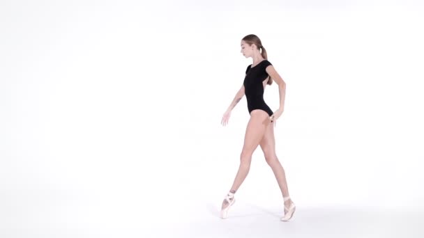 Professionele ballerina dansen ballet op witte Cyclorama. Mooi jong meisje met lang haar dragen zwarte pak geïsoleerd op witte studio achtergrond. — Stockvideo