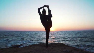 Muhteşem gün doğumunda denizin üzerindeki kayalıklarda yoga yapan kadın. Fitness, spor, yoga ve sağlıklı yaşam tarzı kavramı. Yavaş çekim.