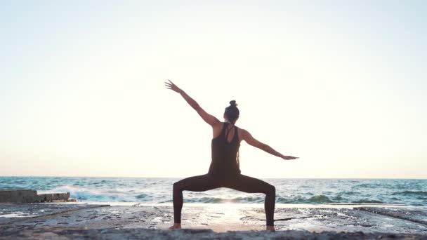 Mujer delgada y saludable haciendo ejercicios de yoga y pilates en superficie de hormigón cerca del mar, sintiendo paz en la naturaleza. Movimiento lento . — Vídeo de stock