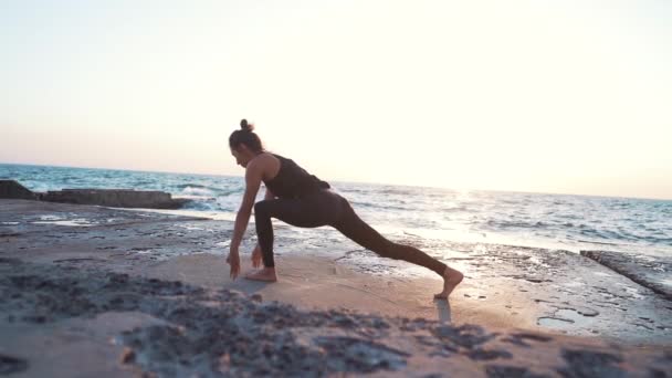 Mujer joven con el pelo rizado en traje negro practicando yoga a la luz del amanecer, escena minimalista. Haciendo asana. concepto de estilo de vida saludable . — Vídeo de stock