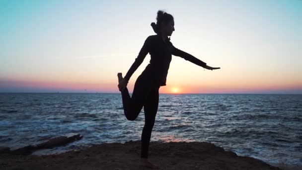 Silhouette of woman practicing yoga on hill over sea at sunset. Meditation. Flexibility workout at nature background. — Stock Video