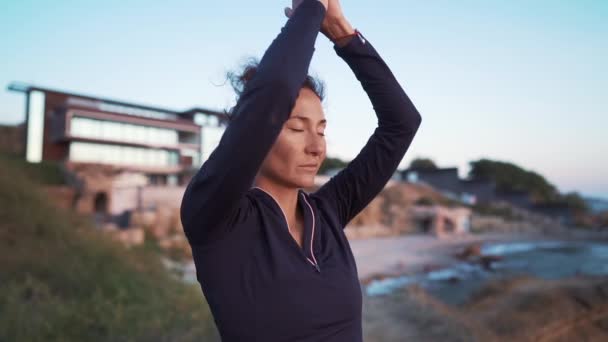 Angenehme Frau macht Gruß an die Sonne bei Sonnenaufgang an der Küste. Yoga, Meditation, gesundes Lebensstilkonzept. — Stockvideo