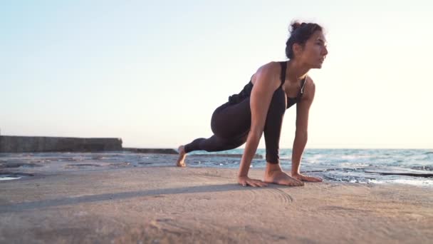 Slanke gezonde vrouw doet yoga praktijk en Pilates oefeningen op betonnen oppervlak in de buurt van zee, het gevoel van vrede in de natuur. Slow Motion. — Stockvideo
